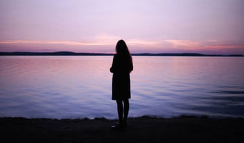 Woman looks out over calm water at sunset