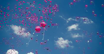 Pink balloons high in air against blue sky and clouds