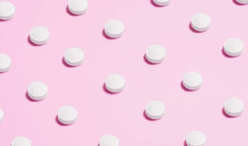 Pills scattered on a pink background