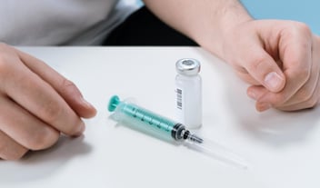 Closeup shot of a vial of medication, a syringe, and hands resting on a table