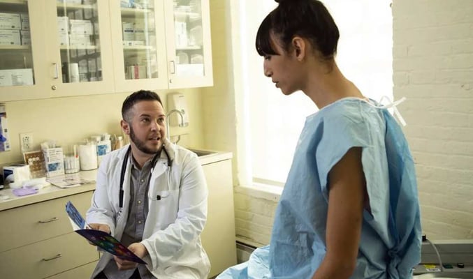 A transgender woman in a hospital gown speaking to her doctor