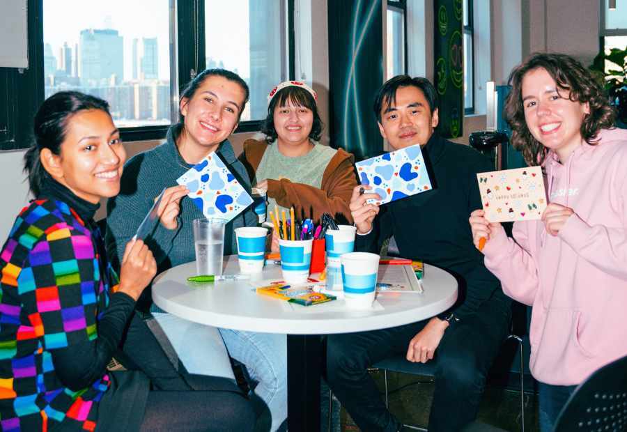 Five coworkers smile around a table, holding up handmade cards they wrote