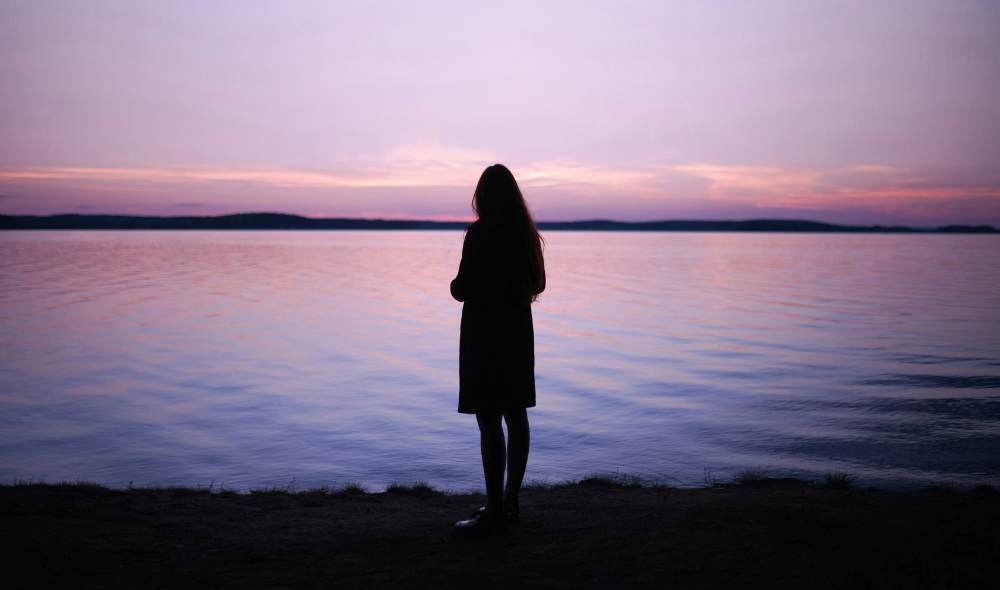 Woman looks out over calm water at sunset