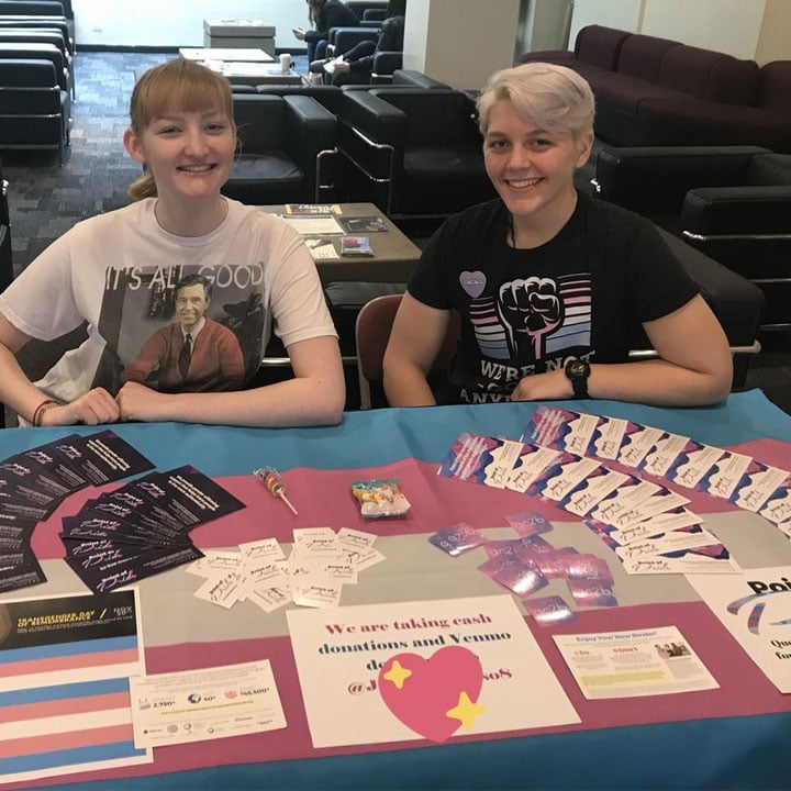 Two young people sit behind a fundraising table Two young people sit behind a fundraising table
