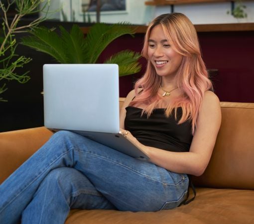 A transfeminine person smiling and using a laptop